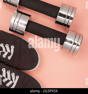 Kleine Metallhanteln und Sneaker zum Training auf rosa Hintergrund. Stockfoto