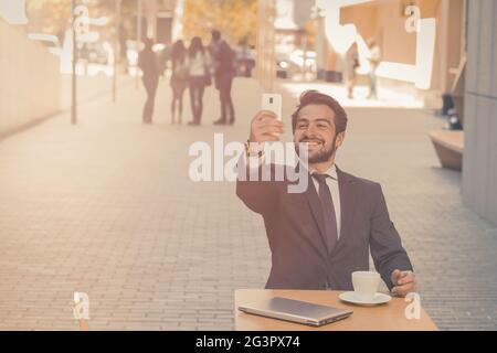 Fröhlicher Geschäftsmann hält ein Online-Meeting mit dem Mobiltelefon ab. Schöner Mann, der mit Partnern spricht oder Selfie nimmt, während er ein sitzt Stockfoto