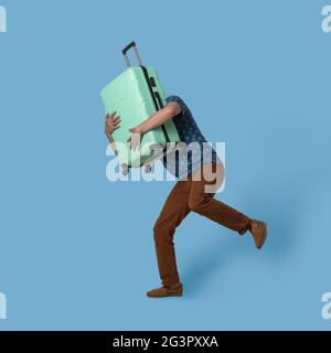 Der Laufmann hält Plastikkoffer vor sich. Kaukasischer Reisender mit hellgrünen Koffer mit Gepäck versucht zu fangen Stockfoto