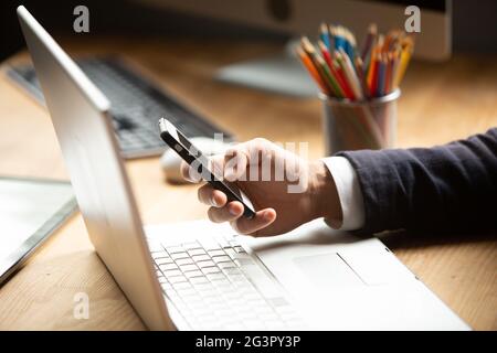 Kaukasischer Mann verwendet Smartphone. Geschäftsmann chattet während der Pause von der Arbeit am Laptop. Nahaufnahme Stockfoto
