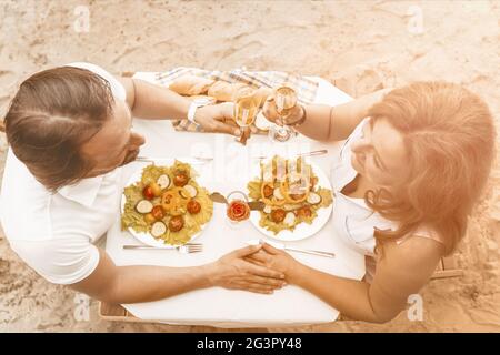 Liebevolle ältere Paare haben romantische Verabdate im Café am Sandstrand im Freien. Mann und Frau mit den Händen sitzen mit Delicious am Tisch Stockfoto