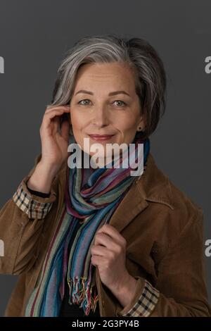 Stilvolle grau Frau charmant lächelt Blick auf die Kamera. Kaukasische Schönheit mittleren Alters in brauner Cordjacke mit Multi gekleidet Stockfoto