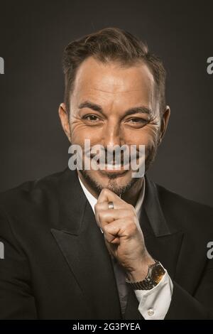 Der attraktive Geschäftsmann lächelt charmant, während er auf die Kamera schaut und seinen Bart mit der Hand berührt. Nahaufnahme Porträt von Stockfoto