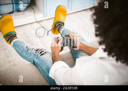 Spieler, der Videospiele spielt. Selektiver Fokus auf männliche Hände, die Tasten am Joystick drücken, um die auf dem Sofa sitzende Spielstation zu spielen. Hi Stockfoto
