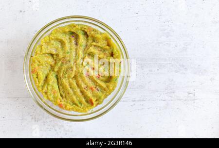 Kleine Glasschüssel mit vorbereiteter Avocado-Guacamole auf einem weißen steinernen Schreibtisch, Blick von oben für Text rechts Stockfoto