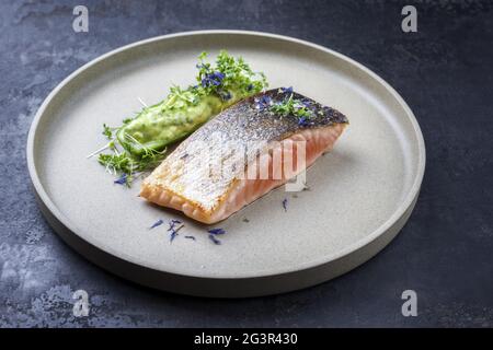 Lachsfischfilet im minimalistischen Design, glasiert mit Avocado und Wasabi creme in einer in Scheiben geschnittenen Gurke als Nahaufnahme auf einem modernen Design pl Stockfoto