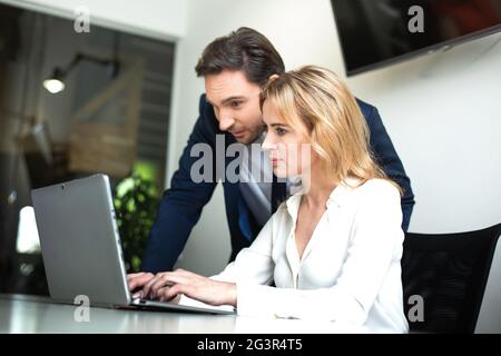 Zwei Büroangestellte, die im Büro mit Computer arbeiten. Geschäftsfrau tippt auf der Tastatur, während ihr Freund, Kollege oder Chef hilft Stockfoto