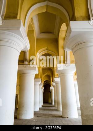 Arkadengang mit hohen, weißen Säulen und gelben Bögen im alten Tirumalai Nayak Palast. Stockfoto