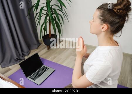 Seitenansicht einer gesunden, achtsamen Frau Sportkleidung meditieren Namaste Hände Online-Kurs Tutorial auf Laptop zu Hause Yoga Training Fitness wo Stockfoto