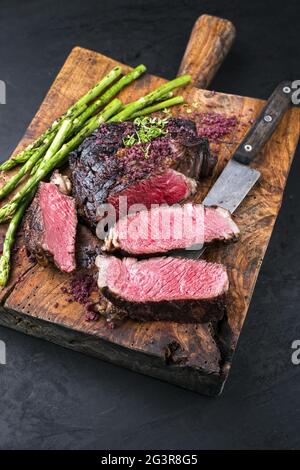 Grillen Sie trocken gealtertes Wagyu-Rindersteak mit grünem Spargel und Rotweinsalz als Nahaufnahme auf einer alten rustikalen Holzschaufel Stockfoto
