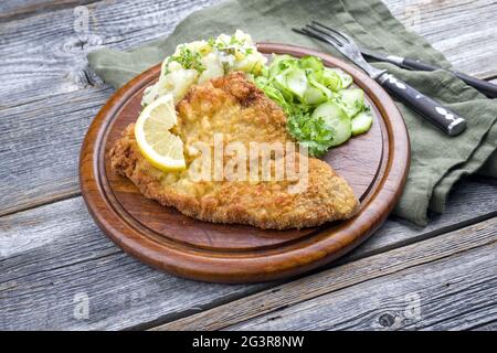 Traditionelles frittiertes Schnitzel mit Kartoffel- und Gurkensalat, das als Nahaufnahme auf einem rustikalen Holzbrett mit Kopierfläche angeboten wird Stockfoto