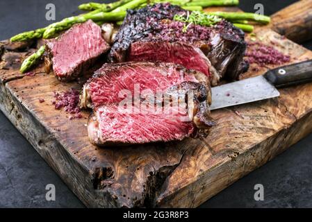 Grillen Sie trocken gealtertes Wagyu-Rindersteak mit grünem Spargel und Rotweinsalz als Nahaufnahme auf einer alten rustikalen Holzschaufel Stockfoto