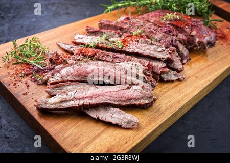 Traditionelles Grillsteak in Scheiben, trocken gereift, Wagyu-Flanke, angeboten mit grünen Kräutern und Chilipulver als Nahaufnahme in modernem Design Stockfoto