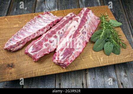 Rohe Schweinelende Rippen St Louis geschnitten mit Kräutern als Nahaufnahme auf einem Holzbrett angeboten Stockfoto