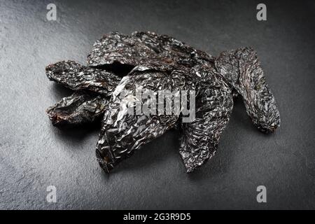 Getrocknetes mexikanisches schwarzes, scharfes Ancho-Chili, das als Nahaufnahme auf einer rustikalen schwarzen Tafel mit Kopierfläche angeboten wird Stockfoto