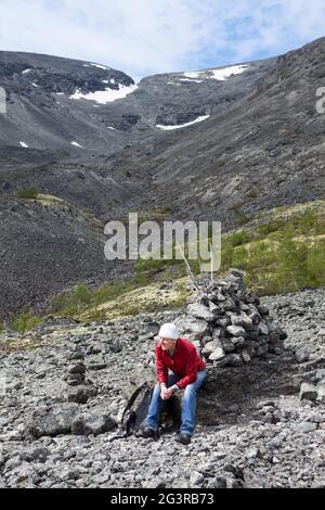 Ein Tourist mit Rucksack sitzt auf einem Stein am Berghang. Ruhen Sie sich während des Kletterns zum Pass aus. Die Chibiny, Russland Stockfoto