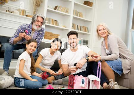 Porträt eines großen glücklichen Mehrgenerationenfamilie Vater Mutter und Großeltern zusammen mit niedlichen kleinen Enkelkind spielen mit Puppenhaus genießen Freizeit im Wohnzimmer zu Hause Stockfoto