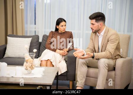 Das junge Ehepaar Frau und Mann diskutieren Missverständnisse in ihren Beziehungen, wenn sie eine Online-Konsultation mit dem Familienpsychologen in Erwägung ziehen, während sie zu Hause im Wohnzimmer sitzen Stockfoto