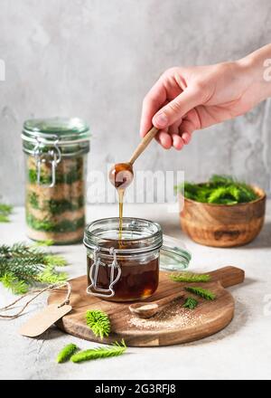 Hand hält einen Holzlöffel mit fließendem hausgemachten Honig aus jungen grünen Fichtenspitzen und Naturzucker. Stockfoto