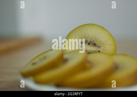 Goldene Kiwi-Scheiben mit gelbem Fruchtfleisch auf weißem Teller in der Küche. Exotische Früchte, gesunde Ernährung Konzept Stockfoto