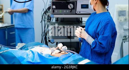 Eine Ärztin im Operationssaal steht mit gekreuzten Fingern in Operationshandschuhen über der Patientin auf dem Operationstisch. Stockfoto