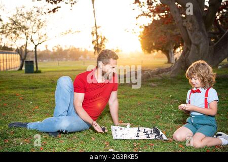 Vater und Sohn spielen Schach auf Gras im Sommerpark, Vaterschaft Stockfoto