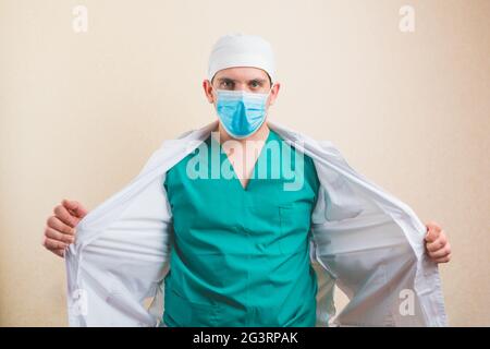 Arzt in schützender medizinischer Maske und grünem Anzug öffnet isoliert sein weißes Fell Stockfoto