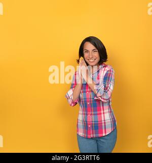 Glückliche Frau faltete Handflächen zusammen lächelnd breit. Junge lachende Modell isoliert auf gelbem Hintergrund Stockfoto