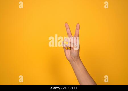 V-Zeichen. Weibliche Hand zeigt zwei Finger oder Friedensgeste. Auf gelbem Hintergrund ausschneiden. Speicherplatz kopieren Stockfoto