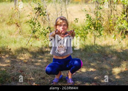 Defocus caucasian preteen Mädchen tun körperliche Bewegung im Park, Wald, im Freien, draußen. Gesunder Wellness-Lebensstil. Kniebeugen mit ausgestreckten Armen. Natur Stockfoto