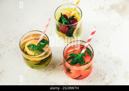 Drei verschiedene gesunde Sommergetränke, Limonade in Gläsern mit Stroh auf weißem Hintergrund. Draufsicht. Stockfoto