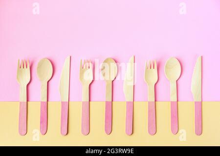 Einweg-Bambuslöffel, Gabeln und Messer auf gelbem und rosa Hintergrund. Zero Waste Konzept. Draufsicht, Kopierbereich. Stockfoto