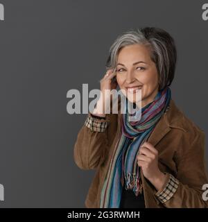 Kreative reife Frau in casual berühren ihre grauen kurzen Haaren. Studio Porträt auf grauem Hintergrund. Platz links kopieren Stockfoto