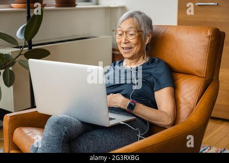 Porträt einer älteren Frau, die lächelt, während sie zu Hause einen Laptop benutzt Stockfoto