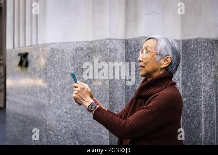 Seitenansicht einer älteren Frau, die ein Smartphone benutzt, während sie an der Wand steht Stockfoto