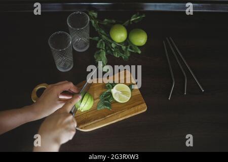 Draufsicht auf eine Frau, die mit einem Messer einen Kalk schneidet, um einen Mojito zu machen Stockfoto