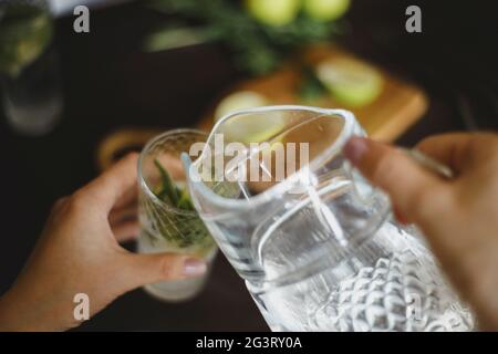Draufsicht auf das Eingießen von Wasser aus einem Krug in ein Glas für Mojito Stockfoto