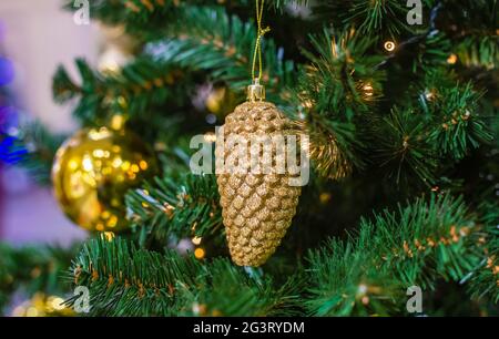 Grüne Zweige eines Weihnachtsbaums mit Tannenzapfen und goldenen Lichtern. Goldene und rote Kugeln schmücken den Weihnachtsbaum. Inneneinrichtung Stockfoto