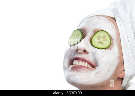 Junge Frau mit Gesichtsmaske, weißem Handtuch auf dem Kopf und Gurkenscheiben auf den Augen Stockfoto