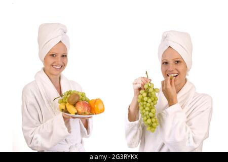 Zwei junge Frauen in weißen Bademänteln, die Trauben und Früchte essen Stockfoto