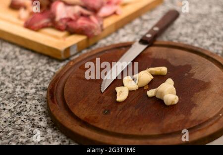 Knoblauch in Scheiben auf einem Holzteller mit rotem Fleisch im Hintergrund. Nahaufnahme. Stockfoto