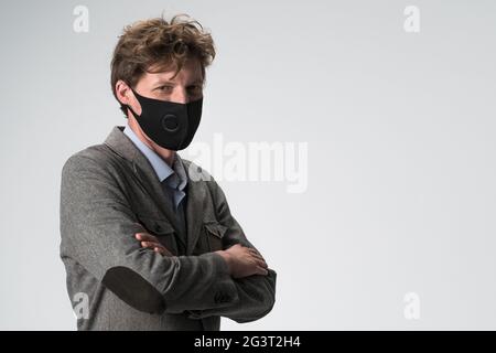 Junger Geschäftsmann in Gesichtsmaske gekreuzte Arme. Selbstbewusster Mann in grauer Jacke posiert auf weißem Hintergrund. Platz auf der rechten Seite kopieren. Stockfoto