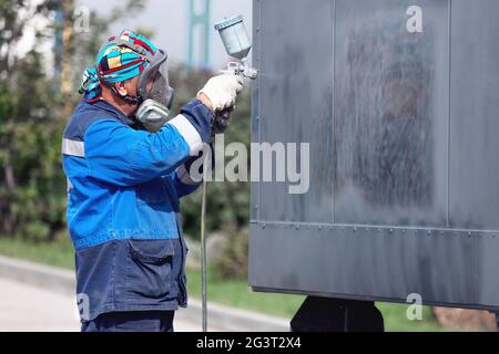 Industriearbeit. Ansaugen von Metallprodukten aus der Kompressorpistole. Ein Arbeiter in Overalls und einer Schutzmaske malt den Körper o Stockfoto