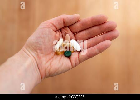 Verschiedene farbige Pillen in einer Hand mit einem hölzernen Hintergrund Stockfoto