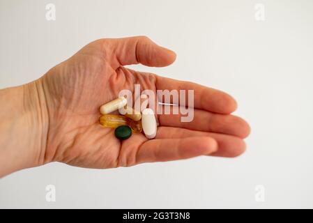 Verschiedene medizinische Pillen oder Nahrungsergänzungsmittel in der Hand von Personen auf weißem Hintergrund Stockfoto