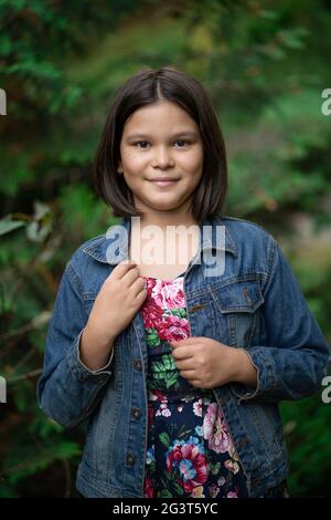 Nettes Mädchen trägt Jeans Jacke posiert im Freien. Mode Brünette Teenager lächelt auf Natur verschwommen Hintergrund Stockfoto