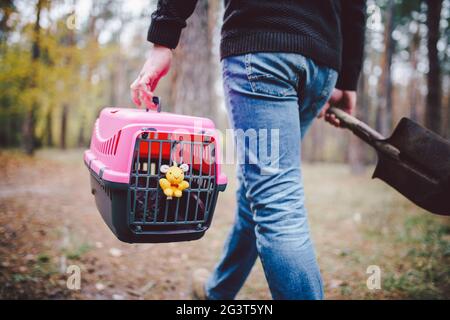 Thema ist der Tod des Haustieres. Rückansicht des Menschen, der auf dem Waldweg läuft und Schaufel in einer Hand zum Graben von Gräbern trägt, und in anderen Stockfoto