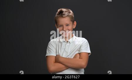 Happy Teenager 10-12 Jahre alt Junge breit lächelt gekreuzte Hände. Emotionen Konzept. Isoliert auf grauem Hintergrund. Speicherplatz kopieren