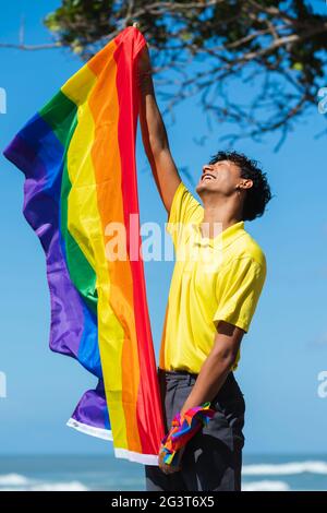 Der junge schwule Mann hält stolz die lgbt-Flagge in den Händen vor dem Meer, inklusive Stockfoto