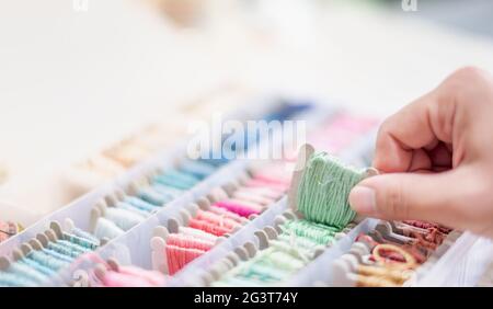 Nahaufnahme Hände der Schneiderin Frau mit hellgrünen Fäden und verschiedenen Farben in der Box auf den Tisch legen und bereiten Sie sich auf die Verwendung mit weißer Baumwolle. Stockfoto